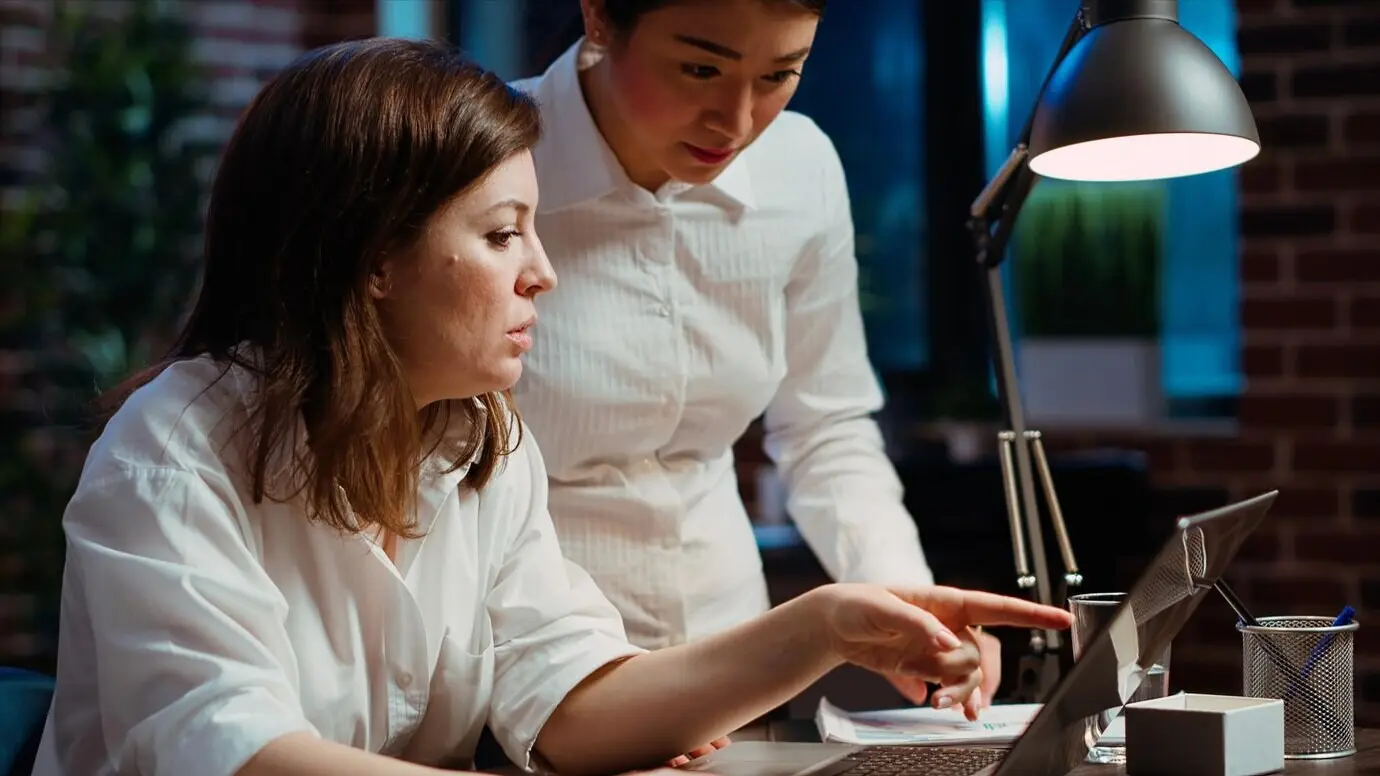 Сотрудник проводит мозговой штурм с руководителем команды, который просматривает на ноутбуке бухгалтерские данные.